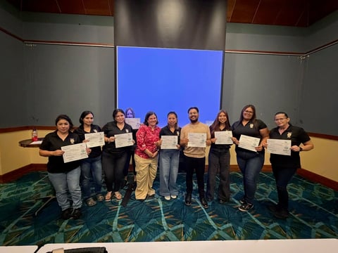 Group of ten people in dark clothing holding certificates standing in front of a large blue screen in an auditorium
