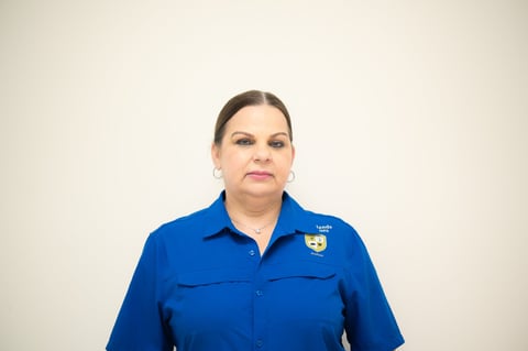 Woman in blue uniform shirt with badge against neutral background, looking at camera
