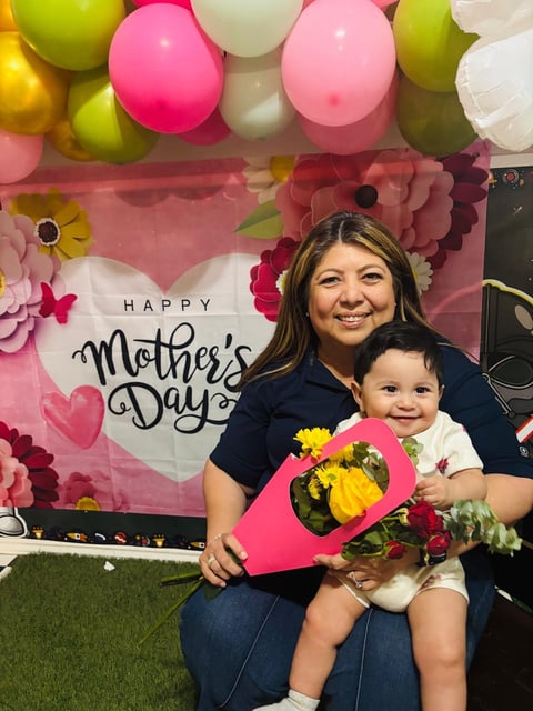 Woman and toddler posing with flowers at Mothers Day celebration backdrop with colorful balloons and floral decorations