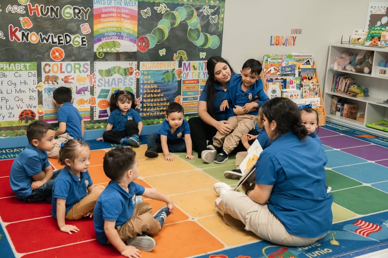 Teacher reading a book to a group of young children sitting on a colorful classroom floor mat
