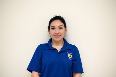 Professional headshot of a woman wearing a blue polo shirt with a crest logo against a neutral white background