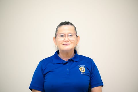 Woman wearing blue polo shirt with logo and glasses, smiling at camera against neutral background