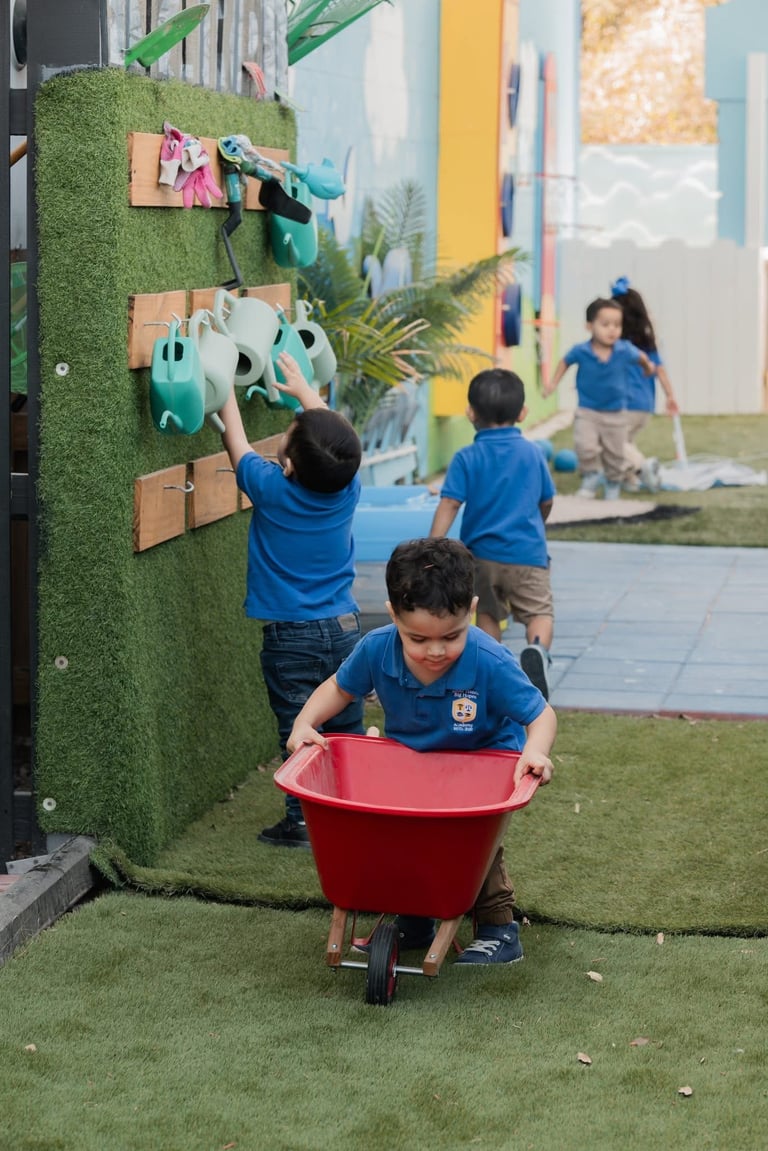 Children in blue shirts playing with a red bucket on artificial grass near an interactive green wall display